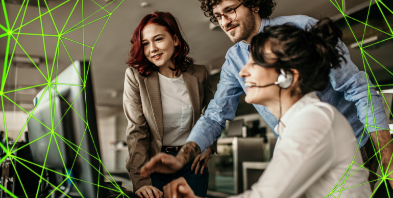 woman sat down with her laptop. 2 people standing and leaning over her to help her with something.